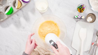 Düz yatıyordu. Adım adım. Vanilyalı Mardi Gras kekleri pişirmek için karışımı elektrikli mikserle karıştırıyorum..