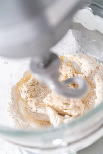 Kneading bread dough in a kitchen mixer with a dough hook to prepare dinner rolls.