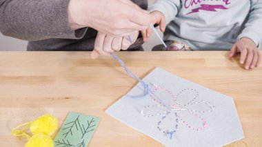 Küçük kız annesiyle el sanatları masasında dikiş dikmeyi öğreniyor..