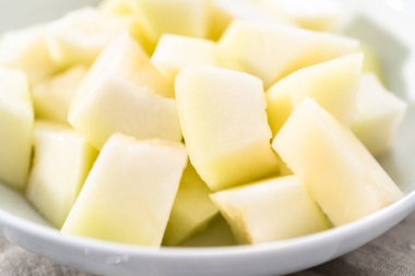 Beyaz bir kasede dilimlenmiş altın çiğ taneli kavun..