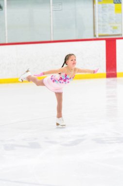 Küçük kız buz pateni pistinde artistik patinaj yapıyor..