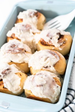 Taze pişmiş tarçınlı rulo, beyaz kremalı, mavi bir tavada..