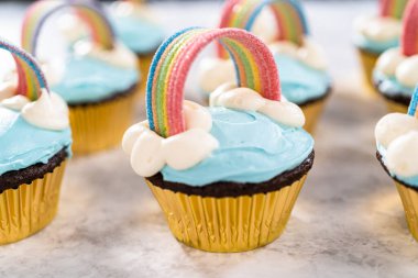 Tek boynuzlu at temalı doğum günü partisi için mavi tereyağlı krema ve gökkuşağıyla süslenmiş çikolatalı kekler..