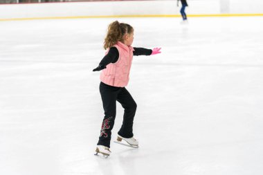 Küçük kız buz pateni pistinde artistik patinaj yapıyor..