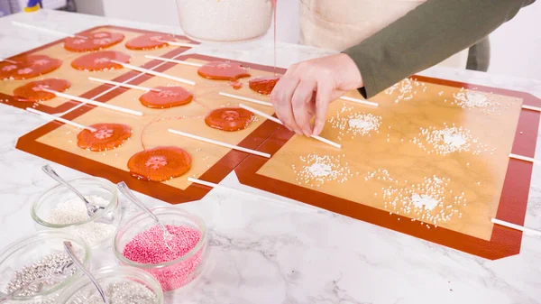 Pouring caramelized sugar on silicone mats to make homemade lollipops.