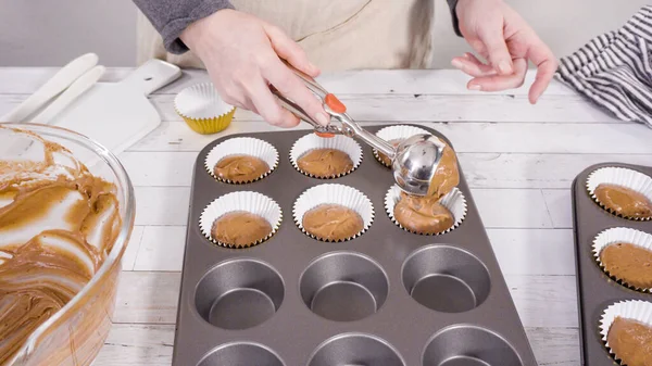 Premium Photo  Scooping pumpkin spice cupcake batter with batter scoop  into a cupcake pan with liners.