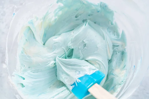 Mixing in blue food coloring into the buttercream frosting.
