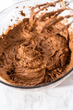 Büyük bir bardakta ıslak malzemeler karıştırarak kırmızı kadife kekler ve beyaz çikolatalı ganache kreması pişiriyorum..