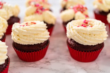 Taze pişmiş kadife kekler, üzerine beyaz çikolata ganache süslemesi serpilmiş..