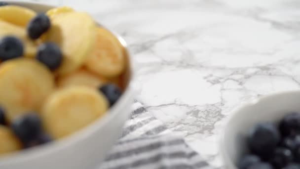 白のボウルに新鮮なブルーベリーと新鮮なミニパンケーキシリアルを作った — ストック動画