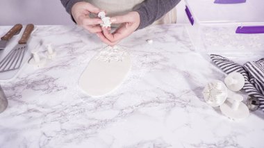 Adım adım. Mermer tezgahın üzerindeki beyaz fondanla kar tanelerini keserek..