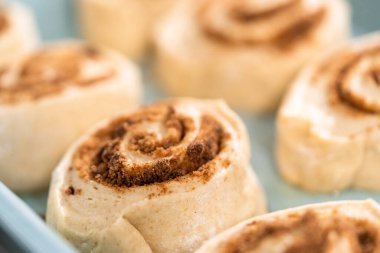 Fırınlanmamış tarçınlı çörekler mavi bir tavada.