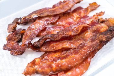 Beyaz tepside pişmiş pastırma şeritleri ve kağıt havlu..