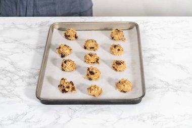 Yumuşak yulaf ezmeli, cevizli, kuru üzümlü kurabiye pişirmek için parşömen kağıdıyla kaplı bir yemek tepsisine hamur kepçesiyle kurabiye pişirmek..