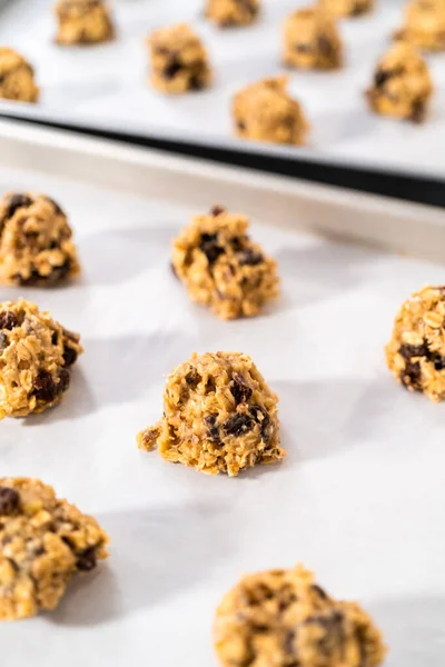 Scooping cookie dough with dough scoop into a baking sheet lined with parchment paper to bake soft oatmeal raisin walnut cookies.