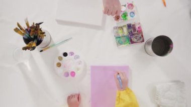 Uzak bir sanat projesi için annesiyle tuvale akrilik boyayla resim yapan küçük bir kız..