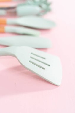 Pembe arka planda ahşap saplı yeni mavi silikon mutfak aletleri..