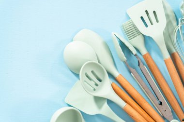 Düz yatıyordu. Mavi arka planda ahşap saplı yeni mavi silikon mutfak aletleri..