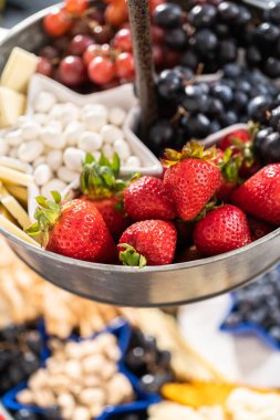 4 Temmuz şarküteri tahtası peynir, kraker, salam ve taze meyve dolu iki katlı bir metal tezgahta.