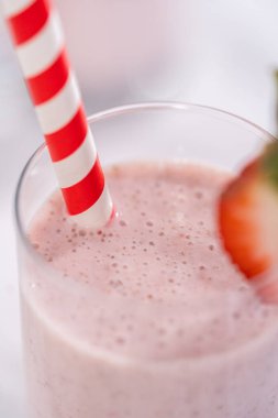 Taze taze çilek ve kağıt kamışla süslenmiş sağlıklı bir kahvaltı muzlu smoothie..
