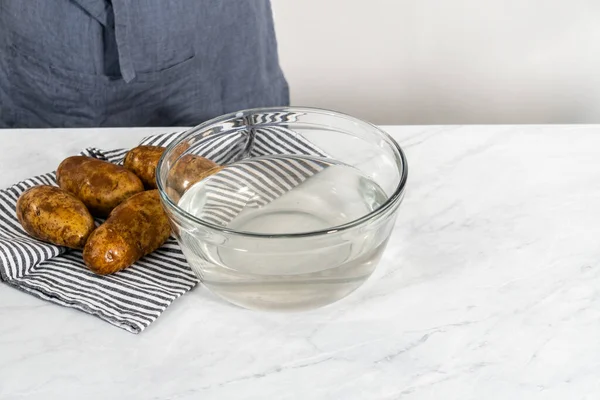 Pressure Cooker Baked Potatoes. Washing raw potatoes in a glass mixing bowl with water.