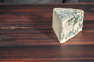 Koyu ahşap arka planda büyük bir dilim mavi peynir..