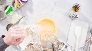 Düz yatıyordu. Adım adım. Vanilyalı Mardi Gras kekleri pişirmek için karışımı elektrikli mikserle karıştırıyorum..