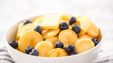 Adım adım. Taze yapılmış mini krep gevreği ve beyaz kasede taze yaban mersini..