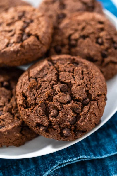 Freshly baked double chocolate chip cookies on a white plate.