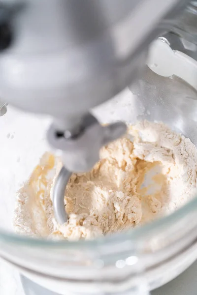 Kneading bread dough in a kitchen mixer with a dough hook to prepare dinner rolls.