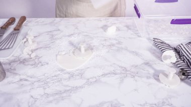 Adım adım. Mermer tezgahın üzerindeki beyaz fondanla kar tanelerini keserek..