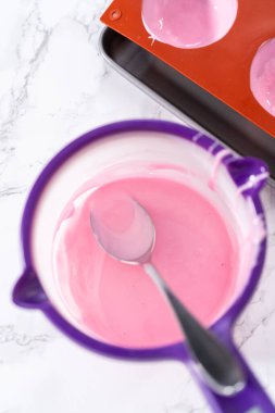 Sıcak çikolata bombaları hazırlamak için silikon çikolata kalıplarını erimiş pembe çikolatayla dolduruyorum..