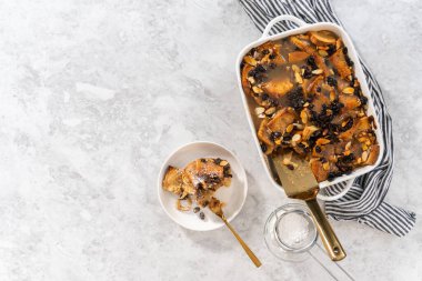 Düz yatıyordu. Beyaz bir güveçte taze ekmek pudingi, üzümlü badem dilimleri servis ediyorlar..