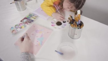 Evde akrilik boyalı bir sanat projesi üzerinde çalışan küçük bir kız..