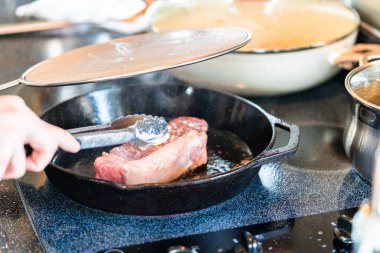 Elektrikli fırının üstünde kızgın demir tavayla New York bifteği kızartıyorum..