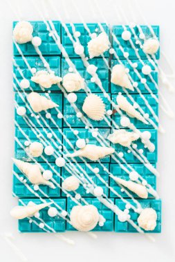 Mini deniz kızı çikolatalarına beyaz çikolata serpiştirilmiş, üzerine beyaz inci şekeri serpiştirilmiş, ve beyaz çikolata deniz kabuklarıyla süslenmiş..