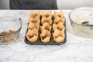 Muzlu yulaf ezmeli kek pişirmek için Lale kağıtlı kek dilimleriyle kaplanmış kek tepsisine hamur kepçesiyle hamur toplamak..