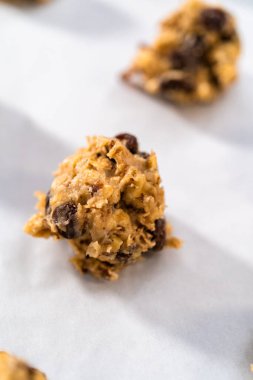 Yumuşak yulaf ezmeli, cevizli, kuru üzümlü kurabiye pişirmek için parşömen kağıdıyla kaplı bir yemek tepsisine hamur kepçesiyle kurabiye pişirmek..