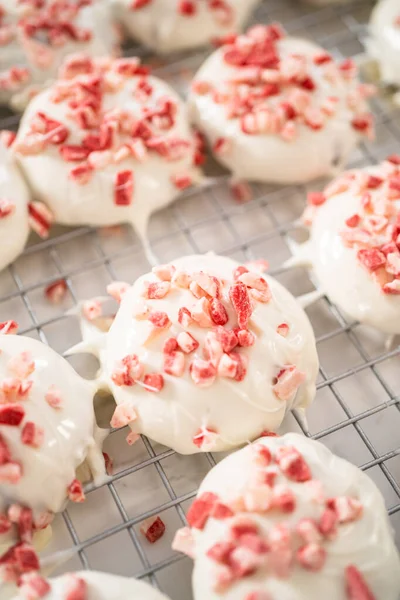 Dipping chocolate cookies into the melted white chocolate to prepare peppermint white chocolate cookies.