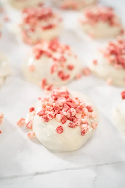 Dipping chocolate cookies into the melted white chocolate to prepare peppermint white chocolate cookies.