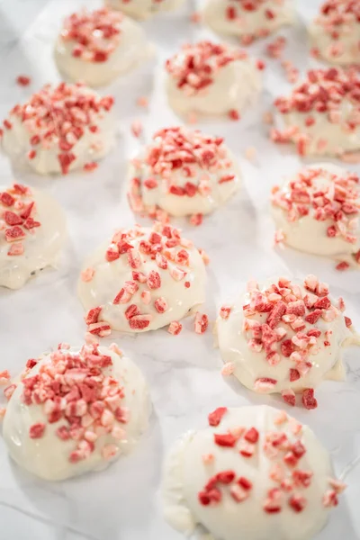 Dipping chocolate cookies into the melted white chocolate to prepare peppermint white chocolate cookies.