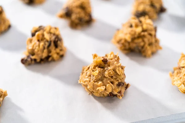 Scooping cookie dough with dough scoop into a baking sheet lined with parchment paper to bake soft oatmeal raisin walnut cookies.