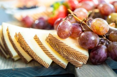 Aperatif olarak sunulan tahtanın üzerinde gurme peyniri, kraker ve meyve var..