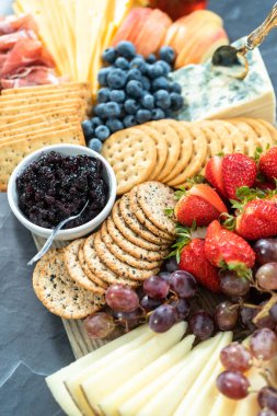 Aperatif olarak sunulan tahtanın üzerinde gurme peyniri, kraker ve meyve var..
