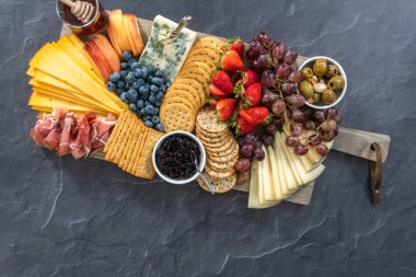 Düz yatıyordu. Aperatif olarak sunulan tahtanın üzerinde gurme peyniri, kraker ve meyve var..