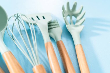 Mavi arka planda ahşap saplı yeni mavi silikon mutfak aletleri..