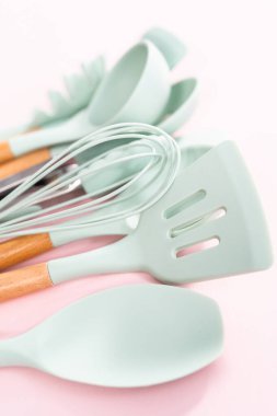 Pembe arka planda ahşap saplı yeni mavi silikon mutfak aletleri..