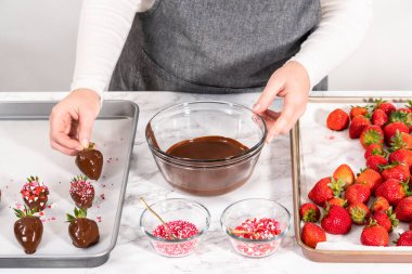 Çikolata kaplı çilekleri hazırlamak için erimiş çikolataya çilek bandırıyorum..