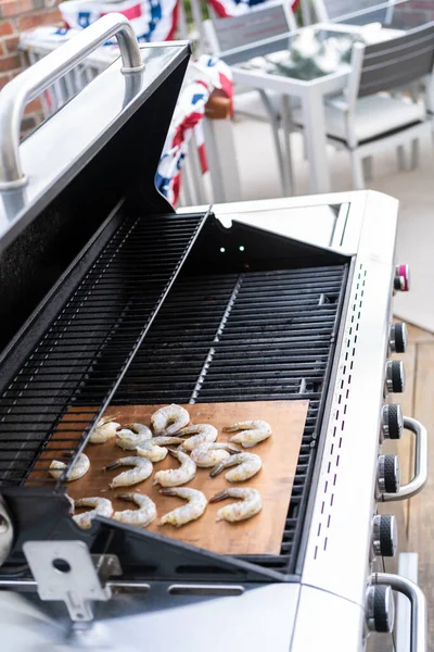 Grilling shrimp on a grill mat over an outdoor gas grill.