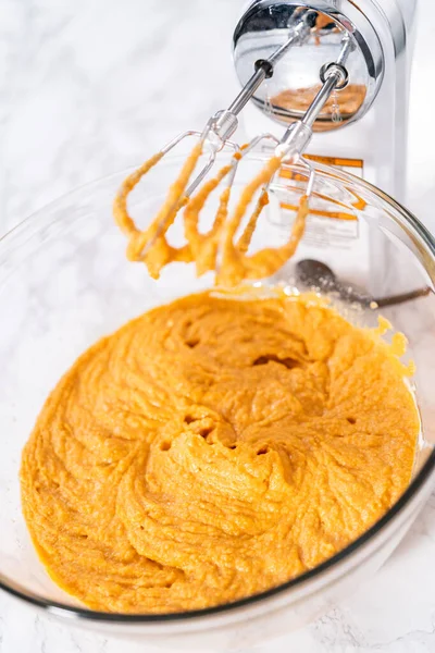 Mixing ingredients in a large glass mixing bowl to bake pumpkin bunt cake.